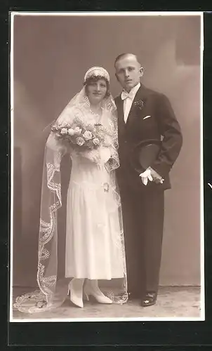 AK charmant blickendes Brautpaar mit Blumen und Zylinder in Hochzeitsmode