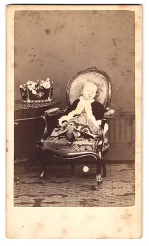 Fotografie Cruces & Gampa, Ort unbekannt, Kleinkind im Kleid mit Mantel auf Sessel sitzend