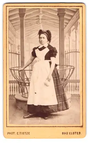 Fotografie E. Tietze, Bad Elster, Portrait junge Bäderfrau in Dienstkleidung an der Sprudelquelle