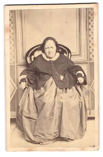 Fotografie unbekannter Fotograf und Ort, betagte Dame im weiten kleid auf Sessel sitzend