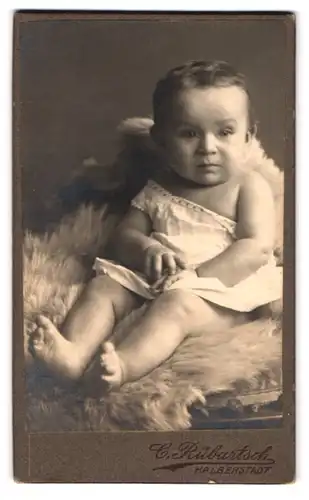 Fotografie Carl Rübartsch, Halberstadt, Breiteweg 15, Portrait süsses Kleinkind im weissen Hemd sitzt auf Fell