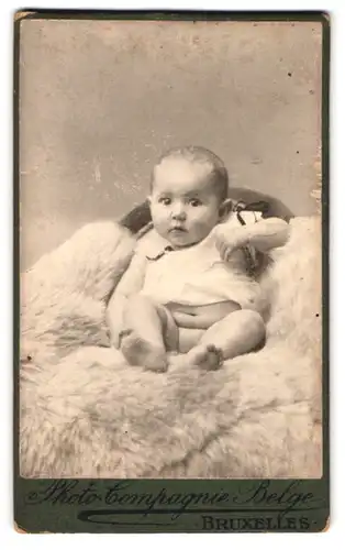Fotografie Photo-Compagnie Belge, Bruxelles, 109, Rue Neuve, Portrait halbnacktes Kleinkind sitzt auf Fell