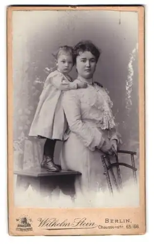 Fotografie Wilhelm Stein, Berlin, Chausseestr. 65, Portrait Mutter im weissen Kleid mit Töchterchen auf dem Tisch