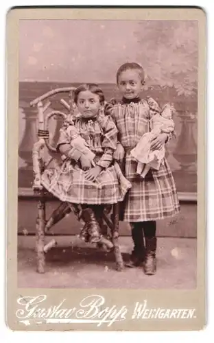 Fotografie Gustav Bopp, Weingarten, Portrait zwei Mädchen in karierten Kleidern mit Puppen im Arm