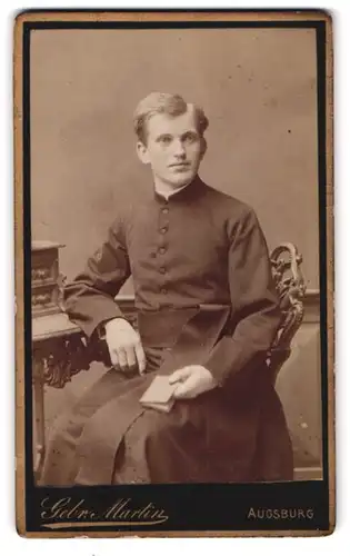 Fotografie Gebr. Martin, Augusburg, Bahnhof-Str., Portrait junger Pfarrer im Talar mit Gebetsbuch in der Hand