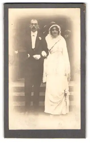 Fotografie unbekannter Fotograf und Ort, Portrait Eheleute im Hochzeitskleid und Anzug mit Zylinder, 1913