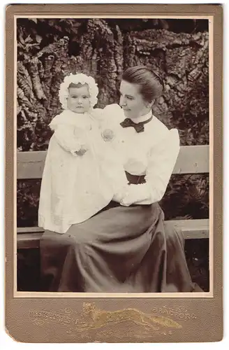 Fotografie A. E. & Fox, Bradford, Portrait Mutter in weisser Bluse mit Tochter im Kleidchen auf einer Bank, Mutterglück