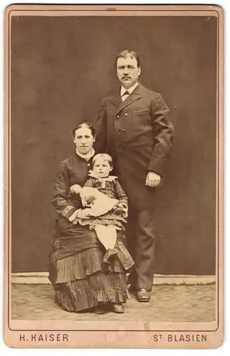 Fotografie Herm Kaiser, St. Blasien, Portrait Mutter und Vater mit Tochter im karierten Kleid auf dem Schoss, Mutterglück