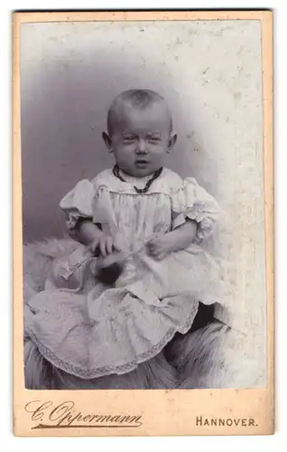 Fotografie Carl Oppermann, Hannover, Engelbostelerdamm 4, Kleinkind in gestreiftem Kleidchen blickt müde in die Kamera