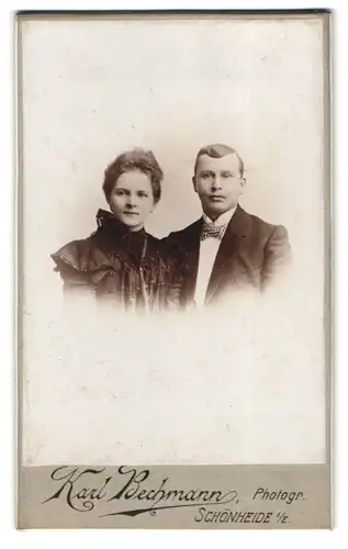 Fotografie Karl Bechmann, Schönheide i. / E., Junges Paar, Dame in schwarzem Kleid und Herr mit karierter Fliege