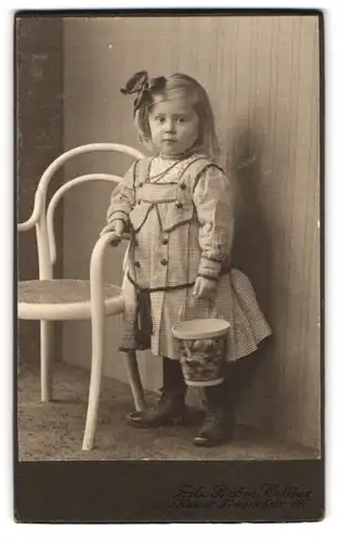 Fotografie Fritz Böhm, Cottbus, Kaiser-Friedrichstr. 127, Kleines Mädchen mit kariertem Kleid und Haarband hält Eimer