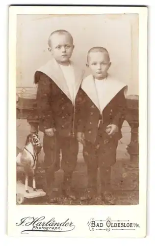 Fotografie J. Harländer, Bad Oldesloe i. H., Portrait zwei Jungen im Matrosenanzug mit Spielzeugpferd