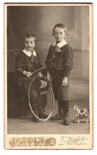 Fotografie Wilh. Gerlich, Neu-Ruppin, Paradeplatz, Portrait zwei modisch gekleidete Jungen mit Reifen u. Spielzeugpferd