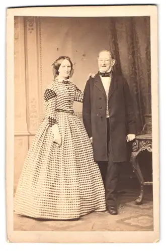 Fotografie unbekannter Fotograf und Ort, Portrait älteres Paar im karierten Kleid und dunklen Anzug mit Fliege