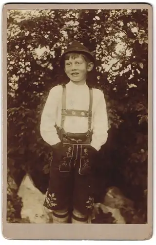 Fotografie unbekannter Fotograf und Ort, Portrait junger grinsender Knabe in Lederhosen mit Hut, bayrische Tracht