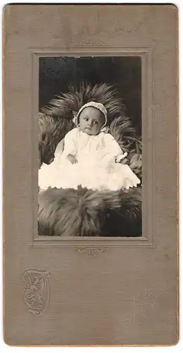 Fotografie unbekannter Fotograf und Ort, Portrait süsses Kleinkind im weissen Kleid sitzt auf Fell