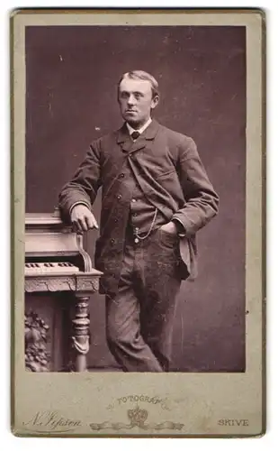 Fotografie N. Jensen, Skive, Herr im Anzug neben einem Klavier