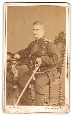Fotografie Th. Jtzerott, Brandenburg a. H., Offizier in Uniform mit Säbel sitzend am Tisch