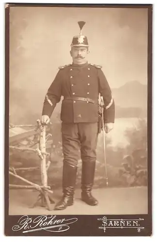 Fotografie R. Rohrer, Sarnen, Portrait Soldat in Uniform mit Hut und Epauletten, Säbel