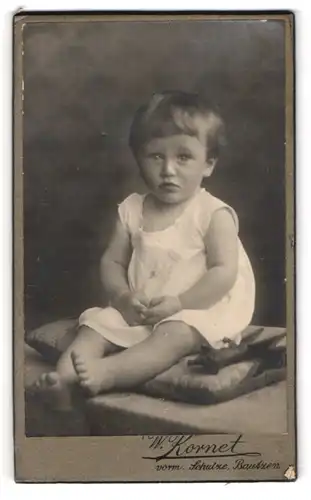 Fotografie W. Kornet, Bautzen, Portrait süsses Kleinkind im weissen Hemd mit nackigen Füssen