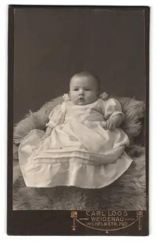 Fotografie Carl Loos, Weidenau, Wilhelmstrasse 79 /2, Portrait süsses Kleinkind im weissen Kleid sitzt auf Fell