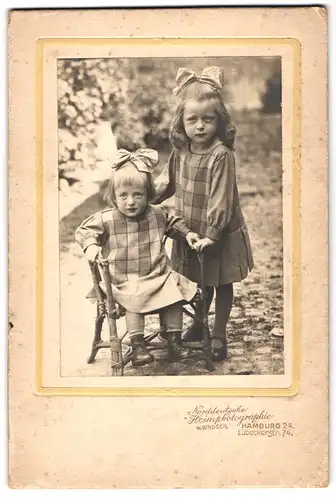 Fotografie W. Bindseil, Hamburg, Lübeckerstr. 74, Portrait zwei niedliche Mädchen in karierten Kleidern mit Haarschleife