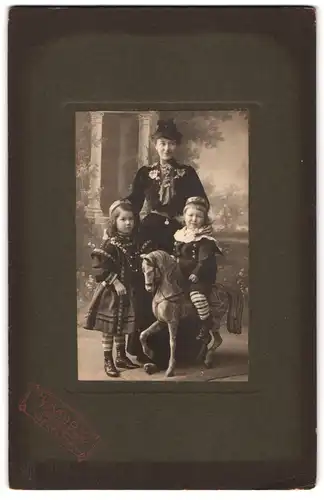 Fotografie H. Kadow, Beuel a. Rh., Portrait Mutter mit zwei Mädchen auf dem Schaukelpferd im Atelier