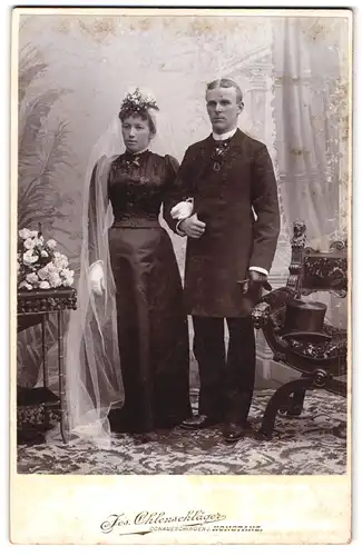 Fotografie Jos. Ohlenschläger, Konstanz, Portrait junges Brautpaar im schwarzen Hochzeitskleid und Anzug nebst Zylinder
