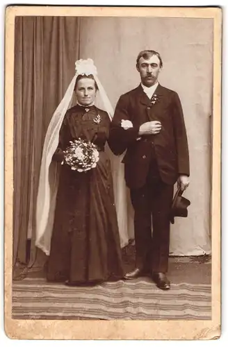 Fotografie Fotograf und ort unbekannt, Portrait Brautleute im schwarzen Hochzeitskleid und Anzug mit weissem Schleier