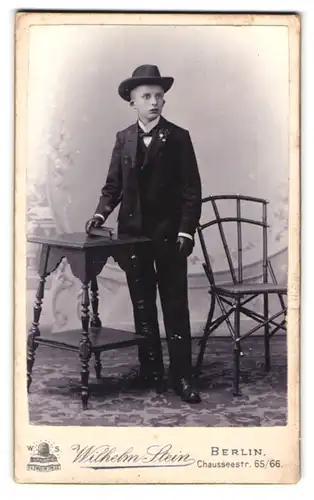Fotografie Wilhelm Stein, Berlin, Chausseestr. 65 /66, Portrait junger Knabe im Anzug mit Hut zur Kommunion
