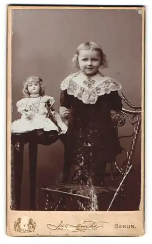 Fotografie J. Fuchs, Berlin, Königstr. 52, Portrait niedliches Mädchen im Kleid mit Ihrer Puppe auf dem Tisch