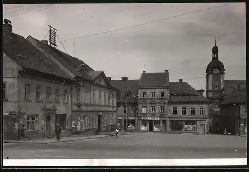 Fotografie unbekannter Fotograf, Ansicht Sluknov, Ladengeschäft mit Vorplatz, Uhrenturm im Hintergrund