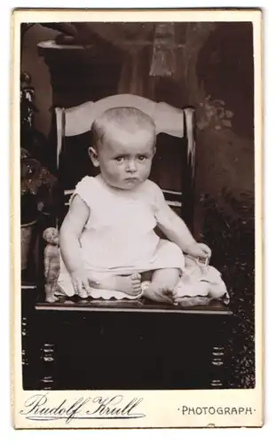 Fotografie Rudolf Krull, Ort unbekannt, Kleinkind mit nackten Füssen und traurigem Blick