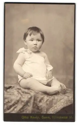 Fotografie Otto Kneip, Bonn, Kölnstrasse 51, Portrait süsses Kleinkind im weissen Hemd mit nackigen Füssen