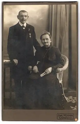 Fotografie Carl Hühner, Auerbach i. V., älterer Herr im Anzug mit Orden an der Brust nebst seiner Frau