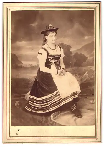 Fotografie unbekannter Fotograf und Ort, Portrait junge Frau im Trachtenkleid sitzend vor einer Studiokulisse