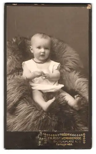 Fotografie Fr. Rose, Wernigerode, Nicolaiplatz 1, Portrait süsses Kleinkind im weissen Hemd sitzt auf Fell