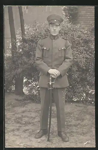 Foto-AK Soldat in Uniform mit Schirmmütze und Degen, Uniformfoto