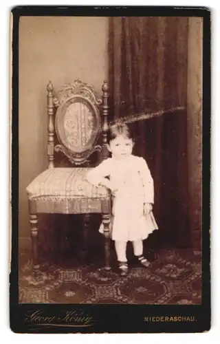 Fotografie Georg König, Niederaschau, Kind in weissem Kleid am Stuhl angelehnt