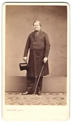 Fotografie M. L. Winter, Prag, Portrait korpulenter Herr im Anzugsmantel mit Stock und Zylinder