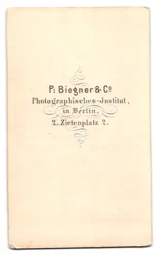 Fotografie P. Biegner & Co., Berlin, Zietenplatz 2, Portrait junged Mädchen im Pünktchenkleid vor einer Studiokulisse