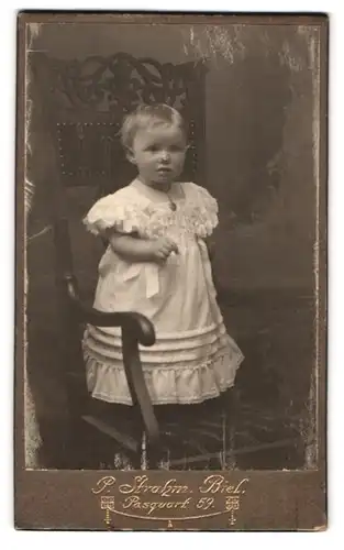 Fotografie P. Strahm, Biel, Pasquart 59, kleines Mädchen im weissen Kleid auf Stuhl stehend