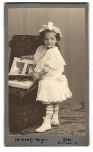 Fotografie Heinrich Meyer, Trier, Simeonstrasse 14, Mädchen in weissem Spitzenkleid mit Haarschmuck am Sessel stehend