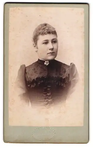 Fotografie L. King, Hanau am Main, Junge Frau im taillierten Puffärmelkleid und Blümchen am Kragen