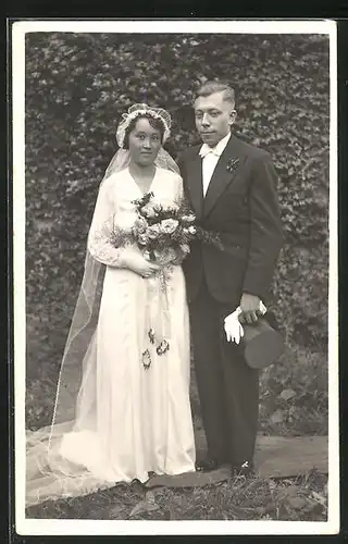 AK Hübsches Brautpaar in eleganter Hochzeitsmode im Garten stehend