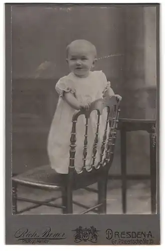 Fotografie Rich Beyer, Dresden, Gr. Plauensche-Strasse 35, Kleinkind in weiss steht glücklich auf einem Stuhl
