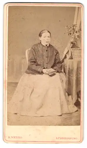 Fotografie R. Wetzig, Ludwigsburg, Stuttgarterstr. 56, Alte Frau in üppigem Kleid sitzt am Tisch