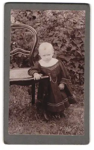 Fotografie W. Lüdecke, Hannover, Kleinkind im übergrossen Kleid vor Brennnesseln posierend