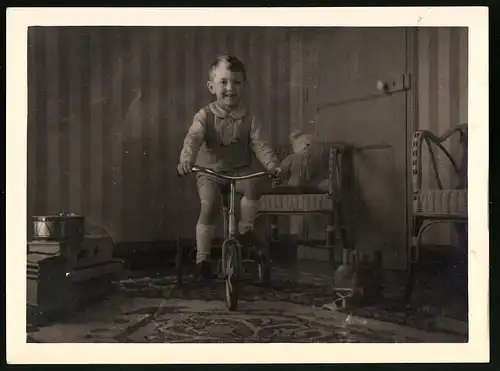 Fotografie glücklicher Knabe auf Dreirad, Teddybär auf Sessel sitzend, Spielzeug-Eisenbahn Lokomotive