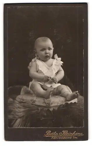 Fotografie Berta Kleinhans, Königsberg i. P., Unterhaberberg 36, Kleinkind in weisser Kleidung sitzt auf Kissen